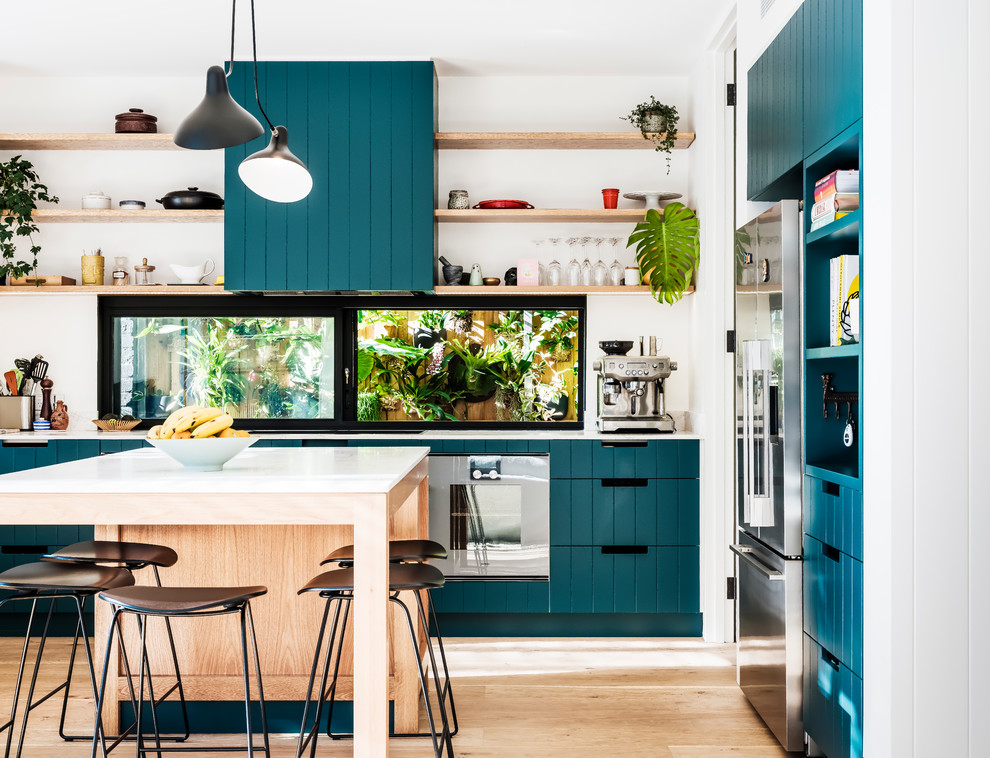 Inspiration for a mid-sized contemporary u-shaped kitchen in Sydney with marble benchtops, white splashback, brick splashback, stainless steel appliances, with island, white benchtop, flat-panel cabinets, turquoise cabinets, light hardwood floors and beige floor.