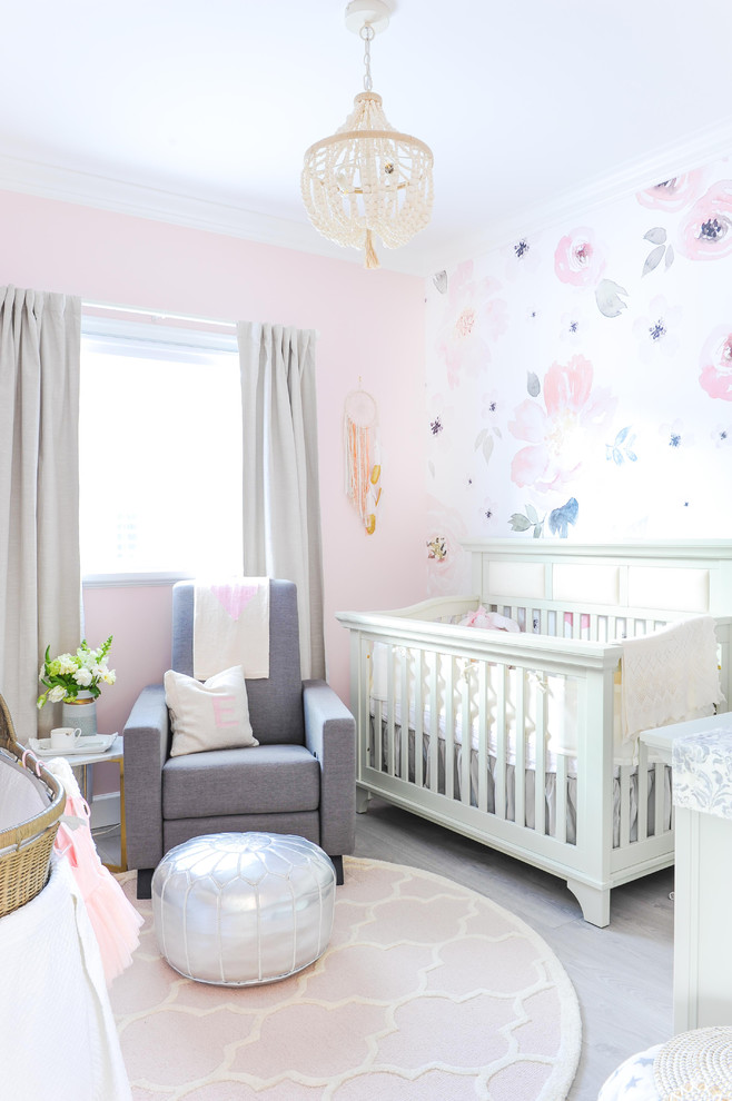 This is an example of a transitional nursery for girls in Vancouver with pink walls, laminate floors and grey floor.