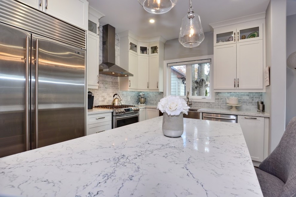 Example of a mid-sized transitional l-shaped brown floor and medium tone wood floor eat-in kitchen design in Toronto with a farmhouse sink, shaker cabinets, white cabinets, quartz countertops, gray backsplash, marble backsplash, stainless steel appliances, an island and white countertops