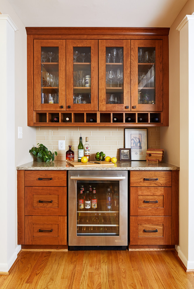 Inspiration for a traditional single-wall home bar in DC Metro with no sink, glass-front cabinets, medium wood cabinets, beige splashback, subway tile splashback and medium hardwood floors.