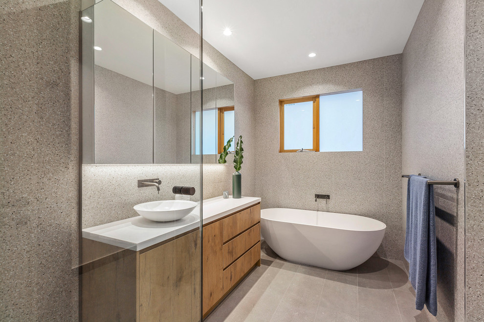 Inspiration for a mid-sized contemporary kids bathroom in Melbourne with medium wood cabinets, a freestanding tub, a corner shower, a wall-mount toilet, gray tile, porcelain tile, grey walls, porcelain floors, a vessel sink, engineered quartz benchtops, grey floor, a hinged shower door and white benchtops.
