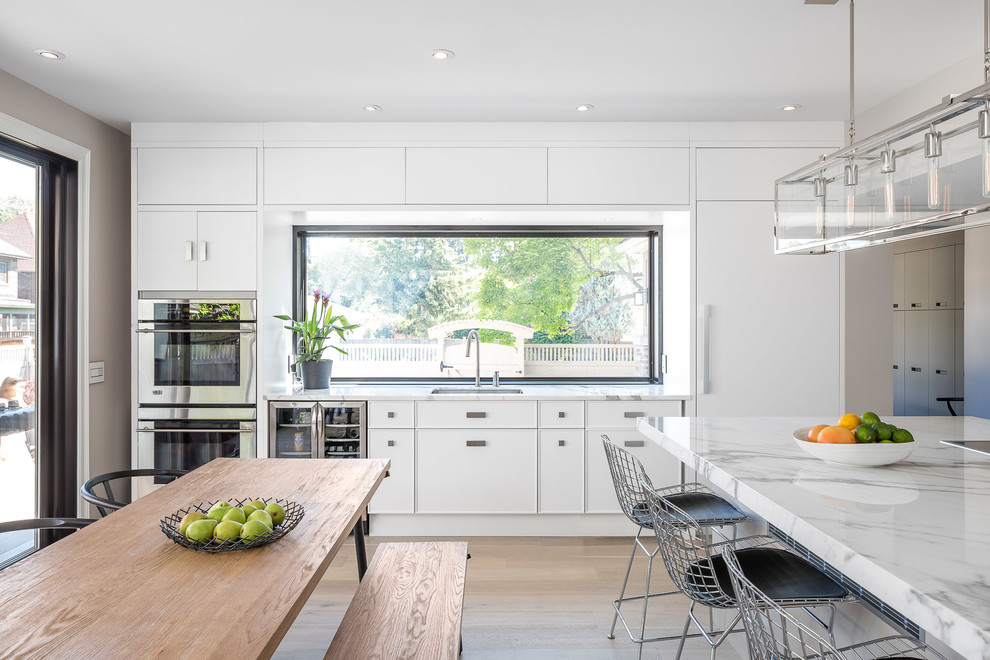 This is an example of a large scandinavian single-wall separate kitchen in Ottawa with a single-bowl sink, flat-panel cabinets, white cabinets, marble benchtops, white splashback, stone slab splashback, stainless steel appliances, light hardwood floors, with island and beige floor.