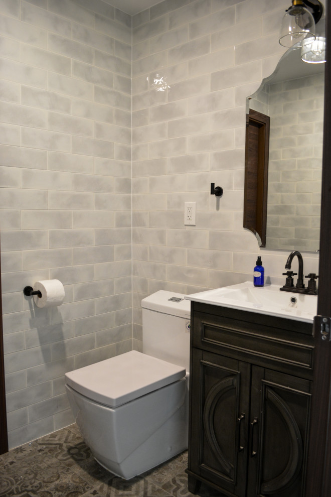 Photo of a mid-sized eclectic powder room in Other with recessed-panel cabinets, grey cabinets, a one-piece toilet, gray tile, subway tile, grey walls, ceramic floors, an integrated sink, grey floor, white benchtops and a freestanding vanity.