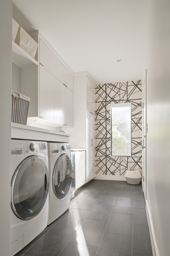 This is an example of a small contemporary laundry room in Austin with flat-panel cabinets, white cabinets, porcelain floors, a side-by-side washer and dryer, grey floor, multi-coloured walls, white benchtop and wallpaper.