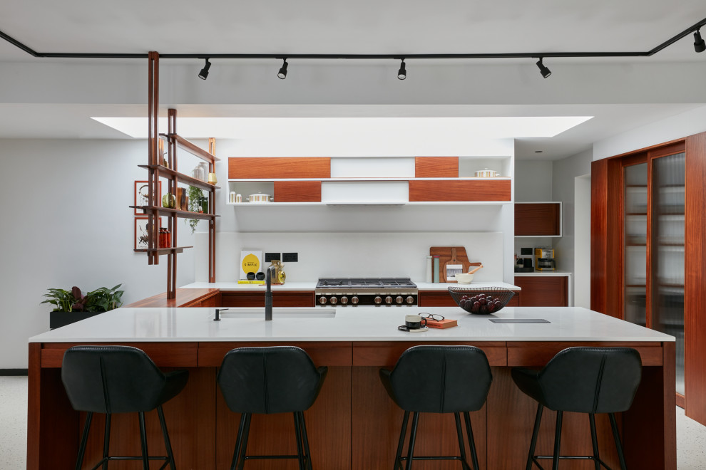 Large midcentury u-shaped open plan kitchen in London with flat-panel cabinets, dark wood cabinets, white splashback, panelled appliances, with island and white benchtop.
