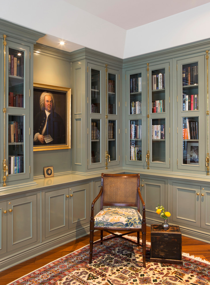 Photo of a mid-sized traditional home office in New York with a library, green walls, medium hardwood floors, a freestanding desk and brown floor.