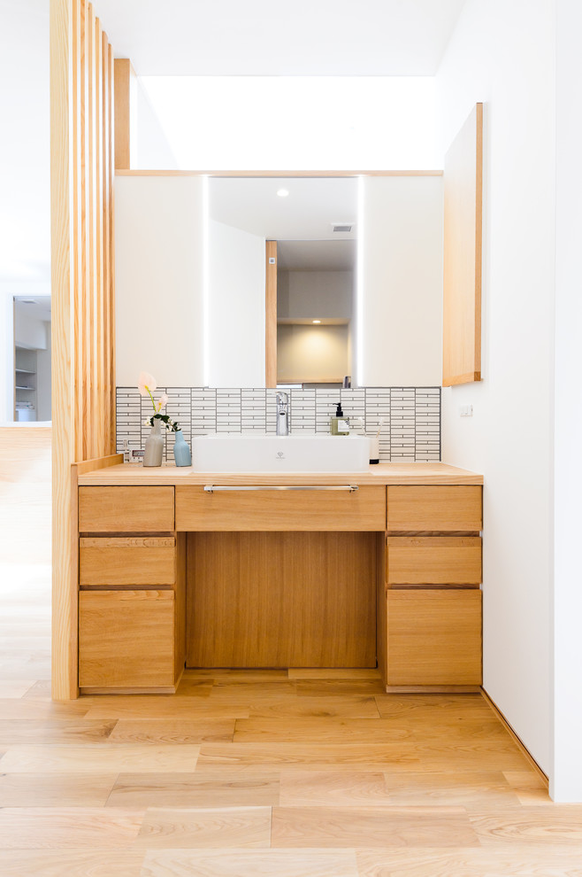 Inspiration for an asian bathroom in Other with flat-panel cabinets, medium wood cabinets, white walls, light hardwood floors, a vessel sink, wood benchtops, brown floor and brown benchtops.