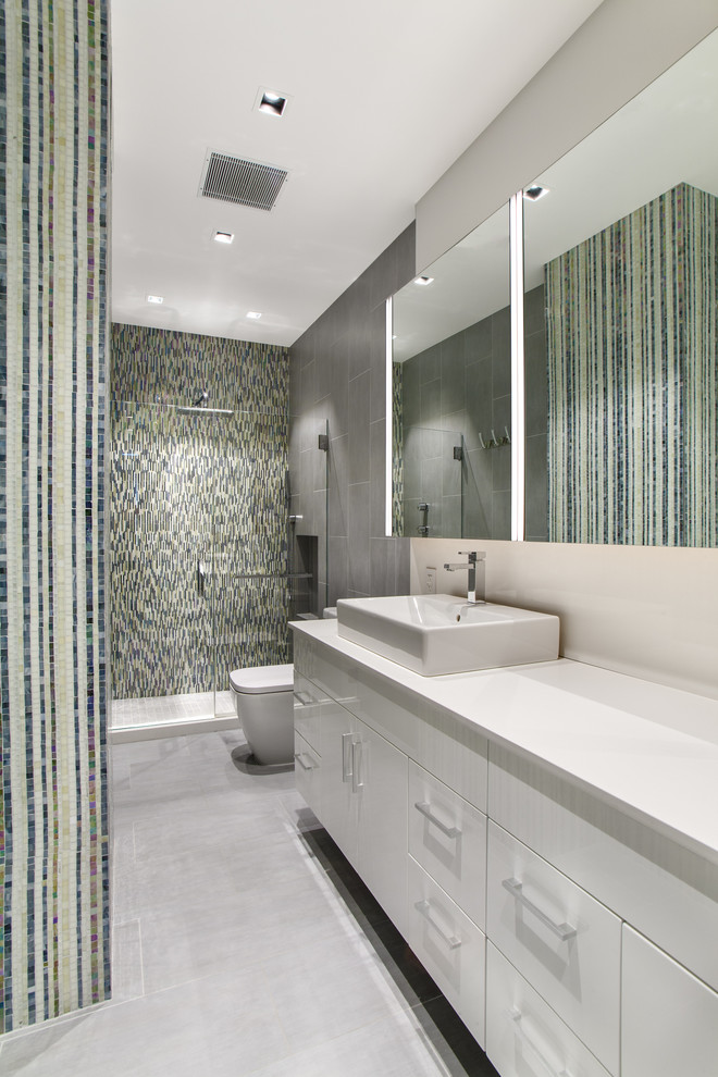 This is an example of a mid-sized modern master bathroom in New York with flat-panel cabinets, white cabinets, an alcove shower, a one-piece toilet, multi-coloured tile, mosaic tile, multi-coloured walls, porcelain floors, a vessel sink and solid surface benchtops.