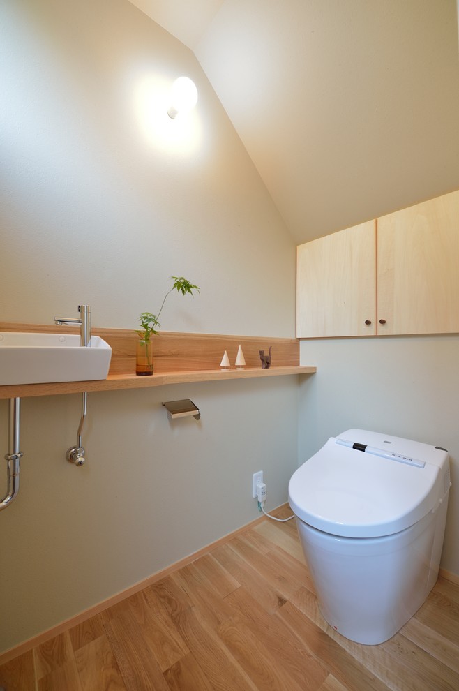 Photo of an asian powder room in Other with flat-panel cabinets, light wood cabinets, green walls, light hardwood floors, a vessel sink, beige floor and brown benchtops.