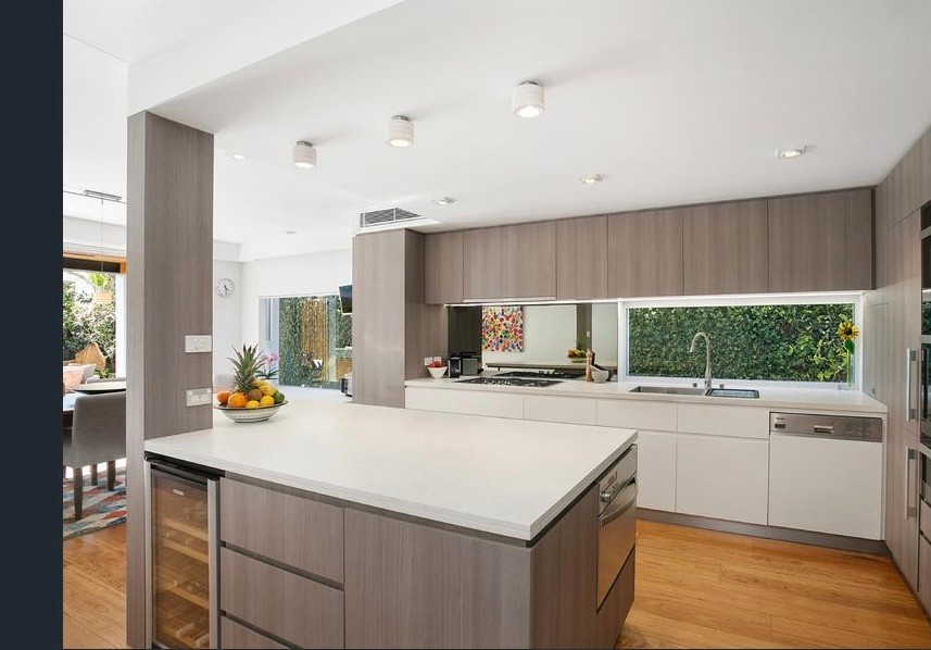 Large galley eat-in kitchen in Sydney with an undermount sink, flat-panel cabinets, light wood cabinets, quartz benchtops, multi-coloured splashback, mirror splashback, stainless steel appliances, light hardwood floors, with island, beige floor and white benchtop.