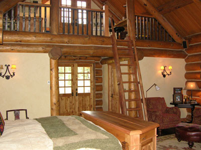 Photo of a large country master bedroom in Other with beige walls, dark hardwood floors, a two-sided fireplace and a stone fireplace surround.