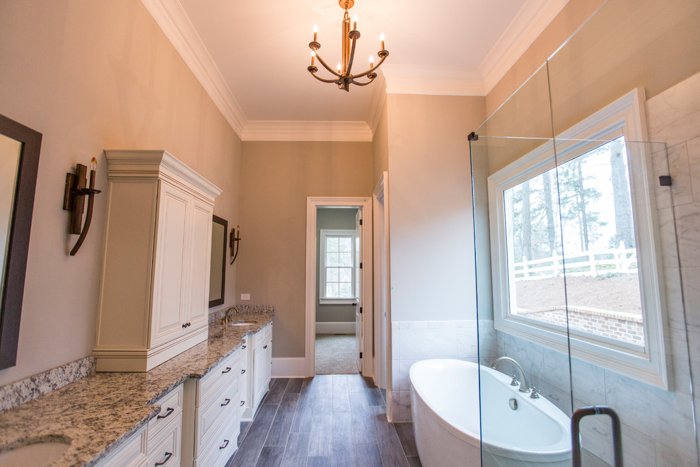 This is an example of a large transitional master bathroom in Atlanta with an undermount sink, raised-panel cabinets, beige cabinets, granite benchtops, a freestanding tub, gray tile, porcelain tile, grey walls and porcelain floors.