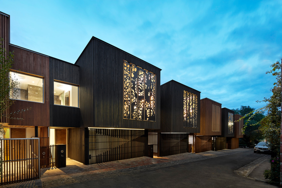 This is an example of a large contemporary two-storey black townhouse exterior in Melbourne with wood siding, a flat roof and a metal roof.