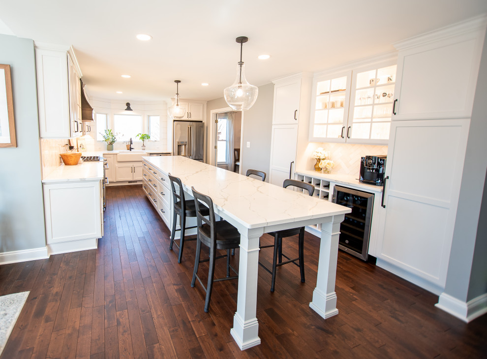 Design ideas for a large country eat-in kitchen in Baltimore with a farmhouse sink, recessed-panel cabinets, white cabinets, quartz benchtops, white splashback, porcelain splashback, stainless steel appliances, dark hardwood floors, with island, brown floor and white benchtop.
