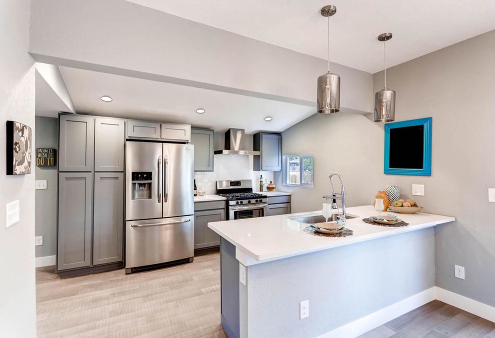 Inspiration for a mid-sized transitional single-wall light wood floor and brown floor enclosed kitchen remodel with an undermount sink, recessed-panel cabinets, gray cabinets, quartz countertops, white backsplash, subway tile backsplash, stainless steel appliances and a peninsula