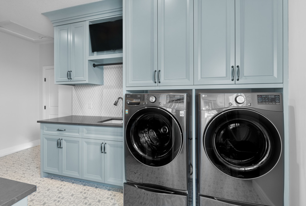Foto på en mellanstor vintage svarta parallell tvättstuga enbart för tvätt, med en undermonterad diskho, luckor med profilerade fronter, blå skåp, granitbänkskiva, vitt stänkskydd, stänkskydd i keramik, klinkergolv i keramik, en tvättmaskin och torktumlare bredvid varandra och blått golv