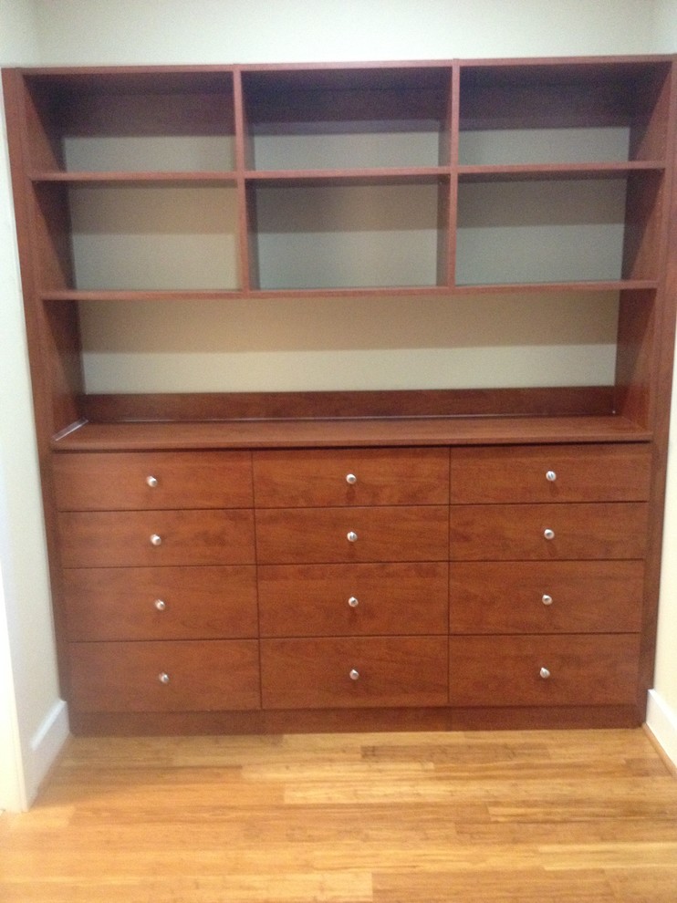 Inspiration for a mid-sized traditional gender-neutral walk-in wardrobe in Other with flat-panel cabinets, medium wood cabinets and light hardwood floors.