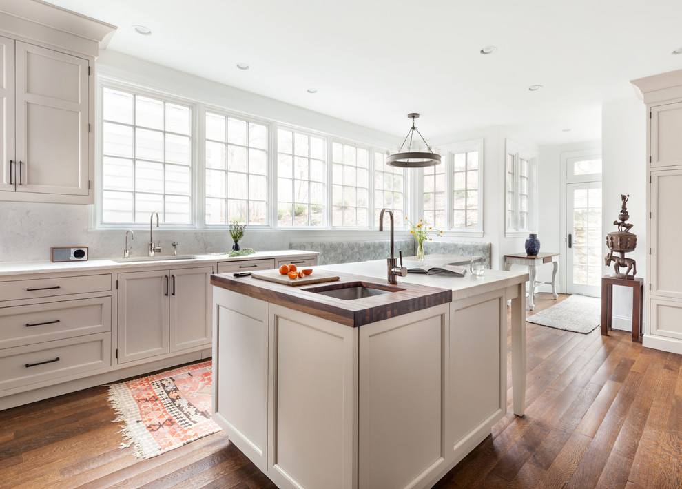 Inspiration for a mid-sized traditional l-shaped eat-in kitchen in New York with an undermount sink, shaker cabinets, beige cabinets, white splashback, stone slab splashback, with island, white benchtop, panelled appliances, dark hardwood floors and brown floor.