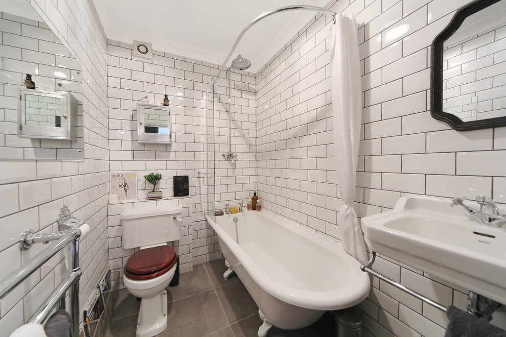 Photo of a small industrial master bathroom in London with a wall-mount sink, a claw-foot tub, an open shower, a two-piece toilet, white tile, ceramic tile, white walls, concrete floors and a shower curtain.