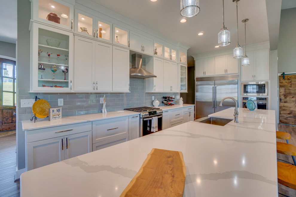 Foto på ett mellanstort funkis vit kök, med en rustik diskho, skåp i shakerstil, vita skåp, bänkskiva i kvarts, grått stänkskydd, stänkskydd i tunnelbanekakel, rostfria vitvaror och en köksö