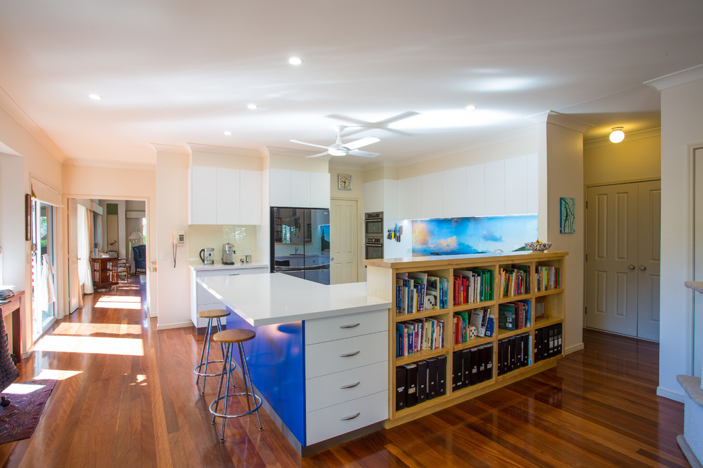Mid-sized beach style u-shaped kitchen pantry in Brisbane with a double-bowl sink, flat-panel cabinets, blue cabinets, quartz benchtops, blue splashback, stainless steel appliances, dark hardwood floors, with island, brown floor and white benchtop.