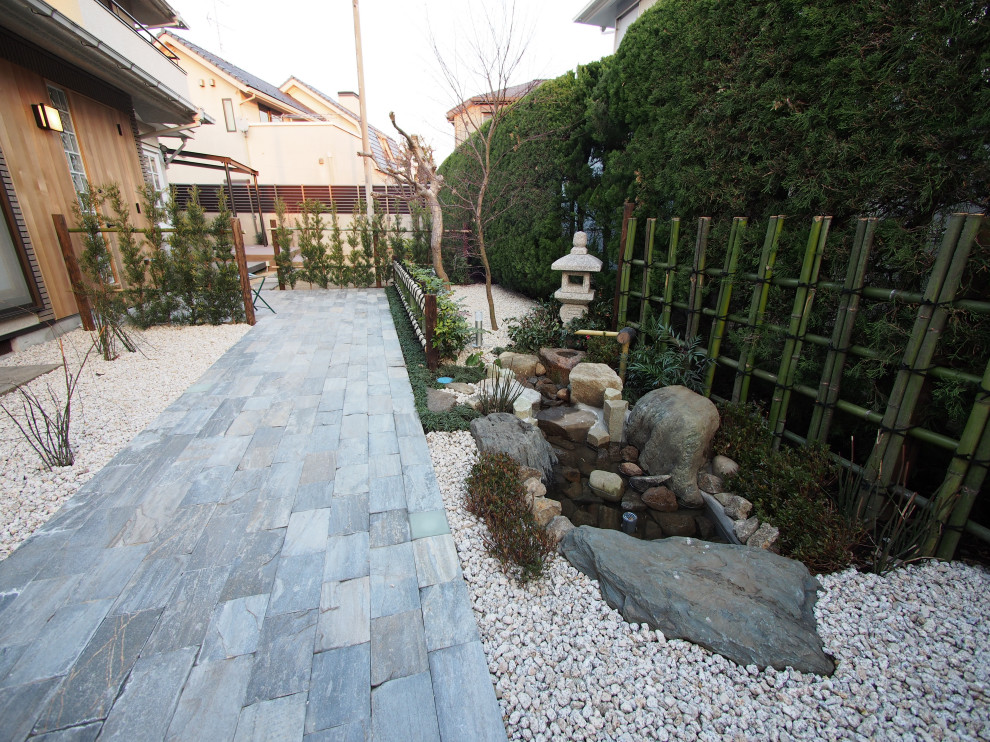 Design ideas for a mid-sized asian front yard full sun formal garden in Tokyo with with rock feature, natural stone pavers and a wood fence.