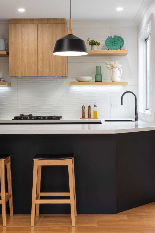 Foto på ett mellanstort funkis vit u-kök, med släta luckor, svarta skåp, bänkskiva i kvarts, vitt stänkskydd, svarta vitvaror och en halv köksö