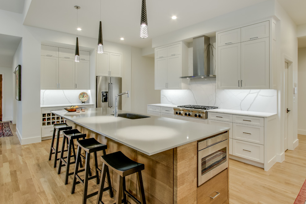 Inspiration for a transitional l-shaped kitchen in Dallas with an undermount sink, shaker cabinets, white cabinets, white splashback, stone slab splashback, stainless steel appliances, light hardwood floors, with island, beige floor and white benchtop.
