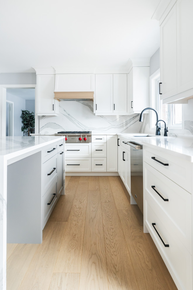 Example of a mid-sized transitional u-shaped light wood floor eat-in kitchen design in Toronto with an undermount sink, shaker cabinets, white cabinets, quartz countertops, white backsplash, quartz backsplash, stainless steel appliances, an island and white countertops