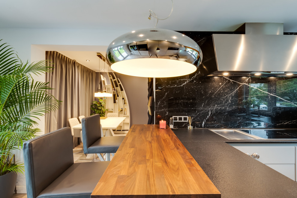 Inspiration for a large traditional u-shaped open plan kitchen in Hamburg with an integrated sink, flat-panel cabinets, white cabinets, solid surface benchtops, black splashback, marble splashback, black appliances, terrazzo floors, a peninsula, multi-coloured floor, black benchtop and recessed.