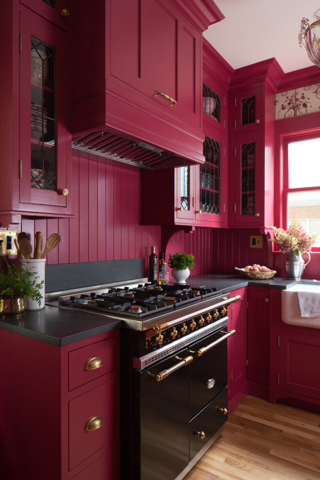 Inredning av ett klassiskt avskilt, litet svart svart l-kök, med en rustik diskho, skåp i shakerstil, granitbänkskiva, rosa stänkskydd, stänkskydd i trä, integrerade vitvaror, ljust trägolv och brunt golv