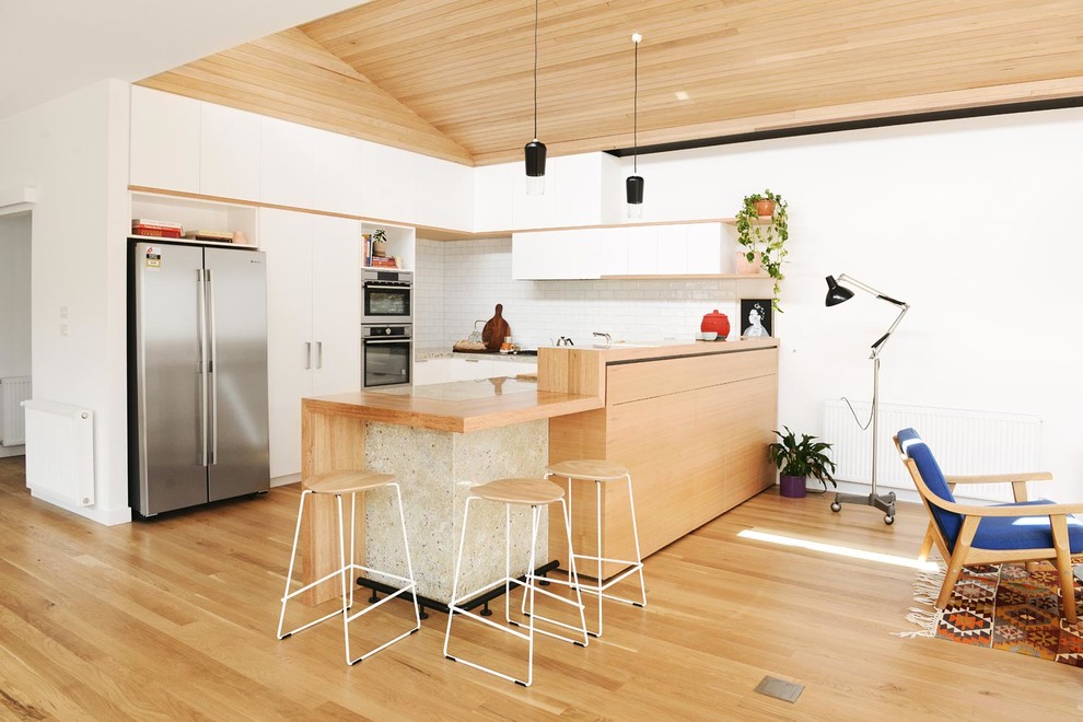 Inspiration for a mid-sized scandinavian u-shaped open plan kitchen in Melbourne with a double-bowl sink, flat-panel cabinets, white cabinets, granite benchtops, white splashback, subway tile splashback, stainless steel appliances and light hardwood floors.