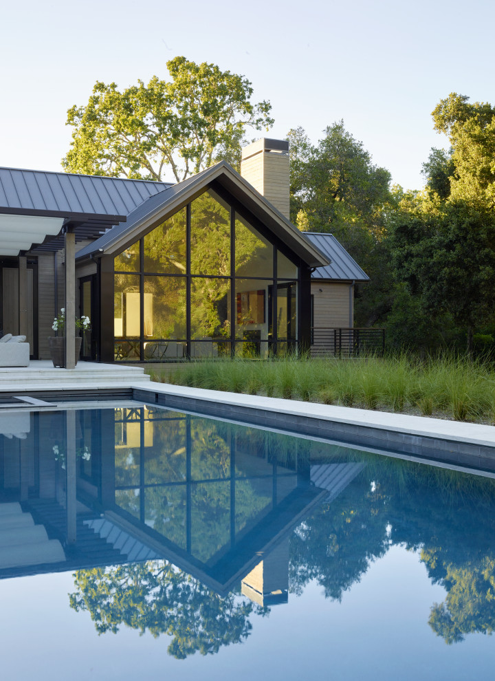 Modelo de piscina infinita de estilo de casa de campo grande rectangular en patio trasero con paisajismo de piscina y adoquines de piedra natural
