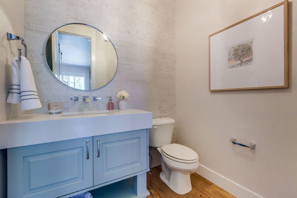 Small transitional powder room in Boise with raised-panel cabinets, blue cabinets, a two-piece toilet, beige walls, light hardwood floors, an undermount sink, solid surface benchtops and brown floor.