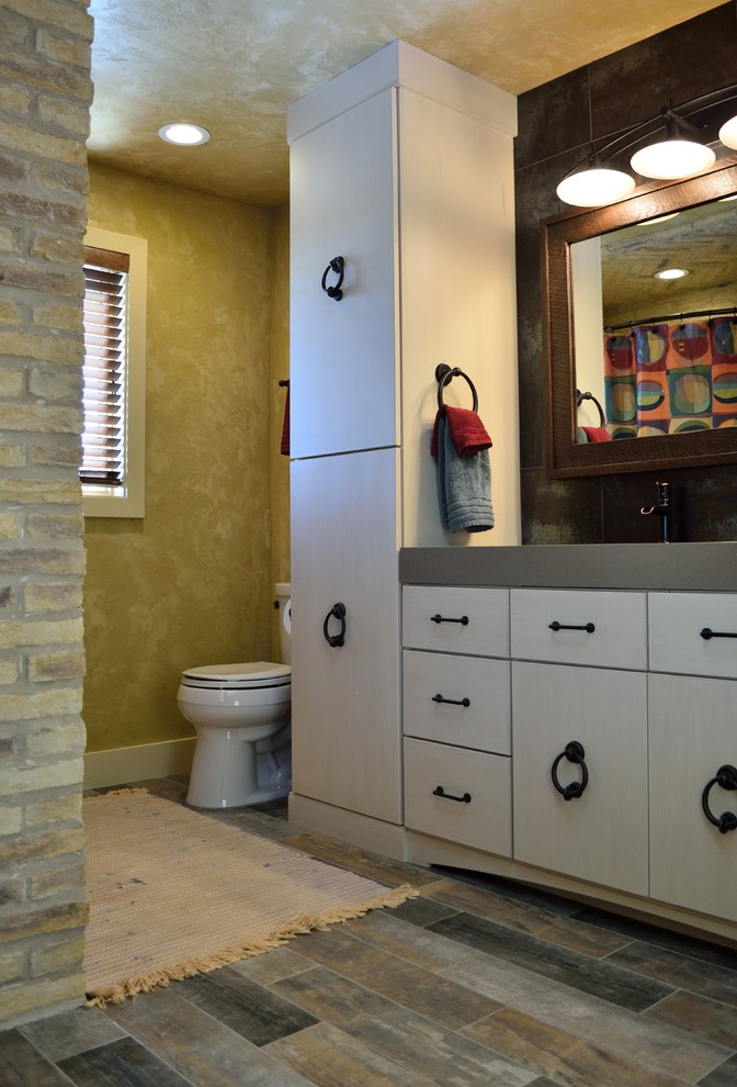 Tub/shower combo - mid-sized rustic beige tile and ceramic tile porcelain tile tub/shower combo idea in Milwaukee with a trough sink, flat-panel cabinets, distressed cabinets, solid surface countertops, a two-piece toilet and beige walls