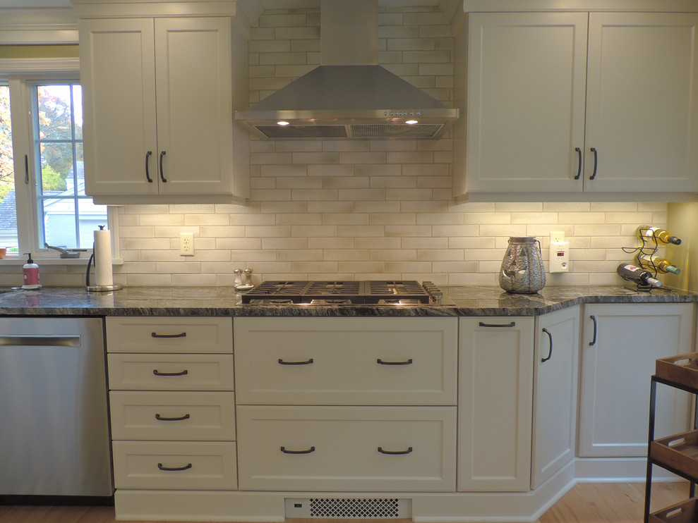 Kitchen - transitional light wood floor kitchen idea with a single-bowl sink, shaker cabinets, white cabinets, granite countertops, white backsplash, ceramic backsplash, stainless steel appliances, an island and black countertops