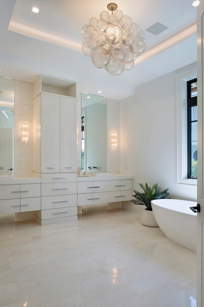 Inspiration for an expansive contemporary master bathroom in Miami with flat-panel cabinets, beige cabinets, a freestanding tub, beige tile, ceramic tile, white walls, marble floors, a drop-in sink, solid surface benchtops, beige floor and white benchtops.