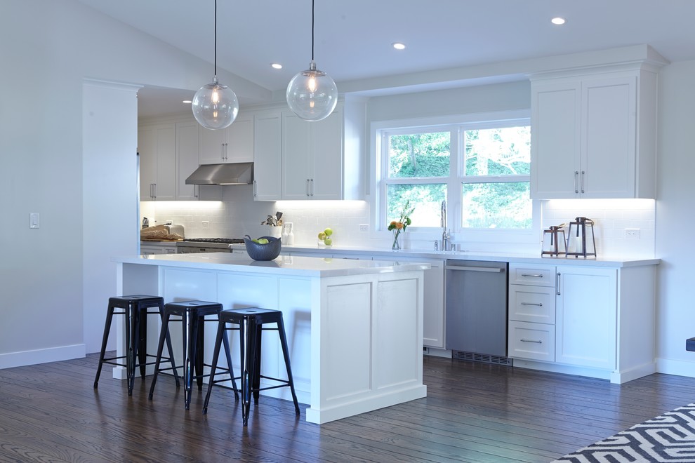 This is an example of a large transitional galley eat-in kitchen in San Francisco with white cabinets, with island, an undermount sink, shaker cabinets, quartz benchtops, white splashback, subway tile splashback, stainless steel appliances and dark hardwood floors.