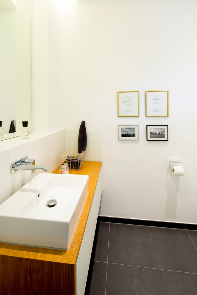 Gästetoilette mit flächenbündigen Schrankfronten, weißen Schränken, Wandtoilette mit Spülkasten, grauen Fliesen, Keramikfliesen, weißer Wandfarbe, Keramikboden, Aufsatzwaschbecken und Waschtisch aus Holz in Dusseldorf