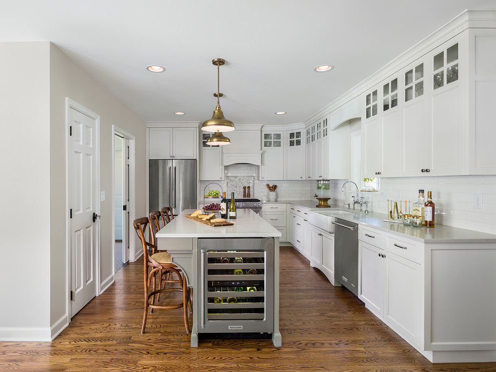 Inspiration for a mid-sized traditional l-shaped eat-in kitchen in Minneapolis with a farmhouse sink, white cabinets, white splashback, subway tile splashback, stainless steel appliances, with island, shaker cabinets, quartzite benchtops and dark hardwood floors.