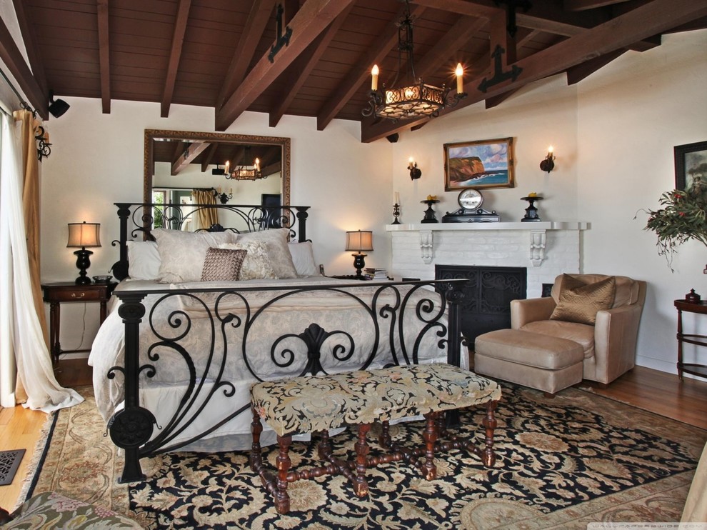 Photo of a large country bedroom in Miami with white walls, light hardwood floors, a corner fireplace and a brick fireplace surround.