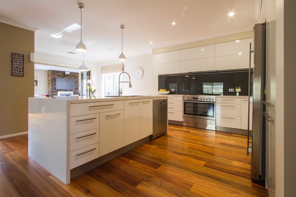 Design ideas for a large modern l-shaped open plan kitchen in Melbourne with flat-panel cabinets, white cabinets, quartz benchtops, grey splashback, glass sheet splashback, stainless steel appliances, medium hardwood floors and with island.