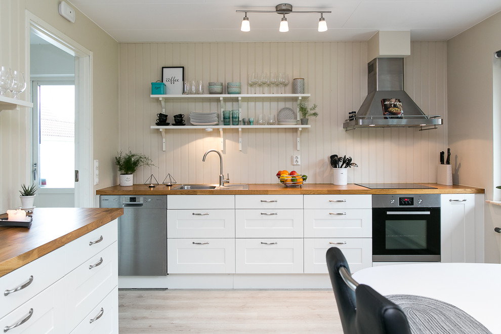 Mid-sized scandinavian l-shaped eat-in kitchen in Malmo with a drop-in sink, shaker cabinets, white cabinets, wood benchtops, beige splashback, stainless steel appliances, light hardwood floors and no island.