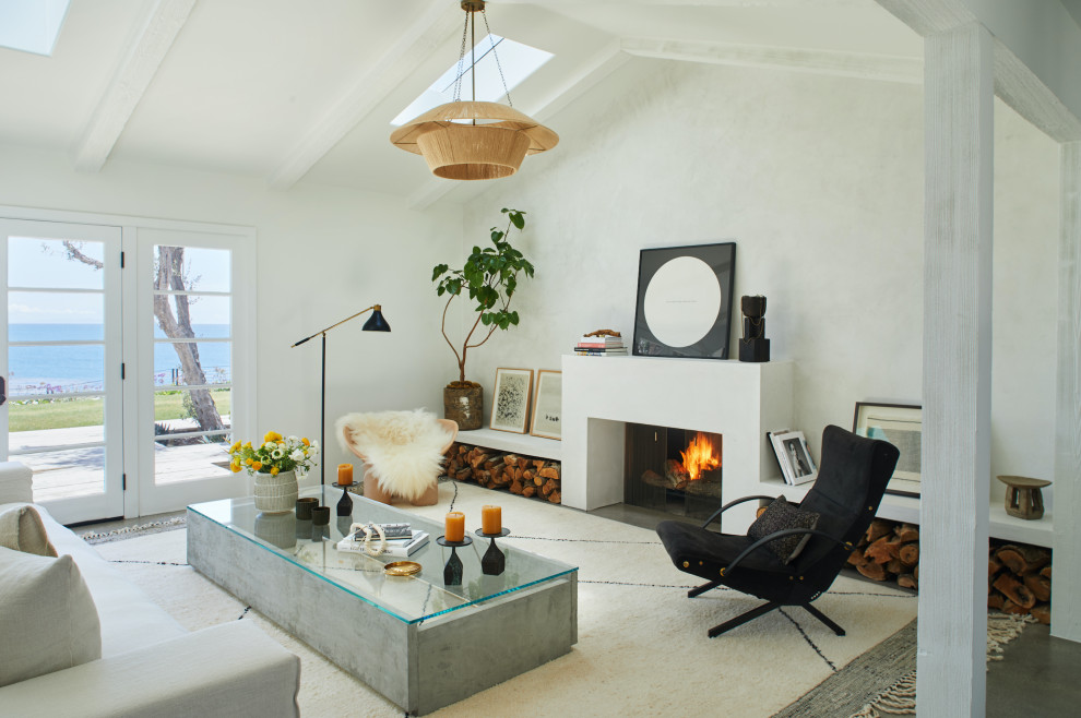 This is an example of a mediterranean living room in Los Angeles with white walls, a standard fireplace, a concrete fireplace surround, grey floor and exposed beam.