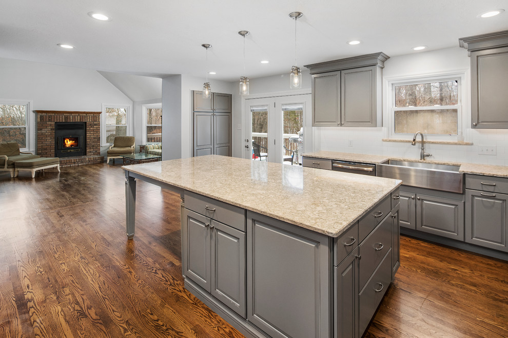 This is an example of a transitional l-shaped eat-in kitchen in St Louis with a farmhouse sink, grey cabinets, granite benchtops, white splashback, subway tile splashback, stainless steel appliances, medium hardwood floors and with island.