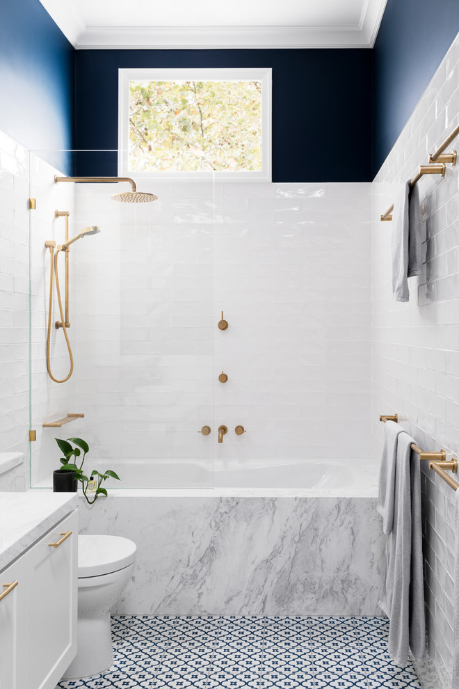 Photo of a mid-sized transitional master bathroom in Melbourne with white cabinets, a shower/bathtub combo, a two-piece toilet, white tile, an undermount tub, blue walls, marble benchtops, blue floor, recessed-panel cabinets, subway tile, porcelain floors, a vessel sink and a hinged shower door.