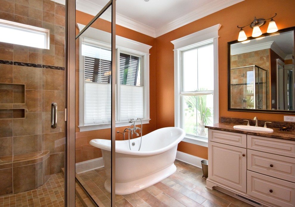 This is an example of a traditional bathroom in Charleston with a freestanding tub, granite benchtops and orange walls.
