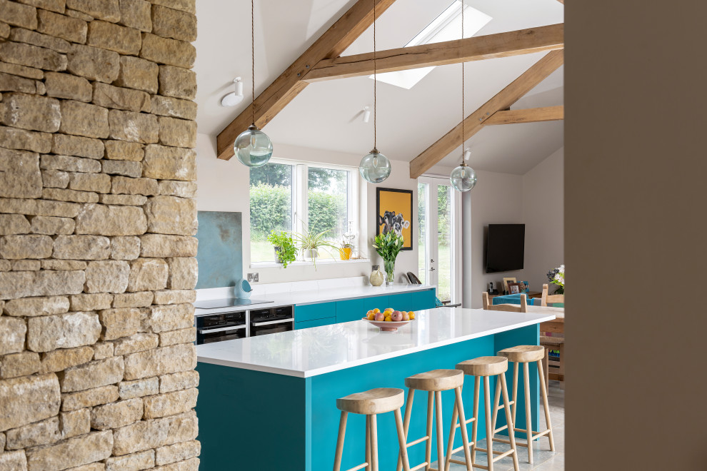 Photo of a farmhouse galley kitchen in Wiltshire with flat-panel cabinets, turquoise cabinets, black appliances, an island, grey floors and white worktops.