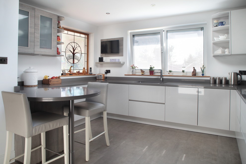 Photo of a contemporary u-shaped kitchen in Buckinghamshire with an undermount sink, flat-panel cabinets, white cabinets, concrete floors, a peninsula, grey floor and grey benchtop.