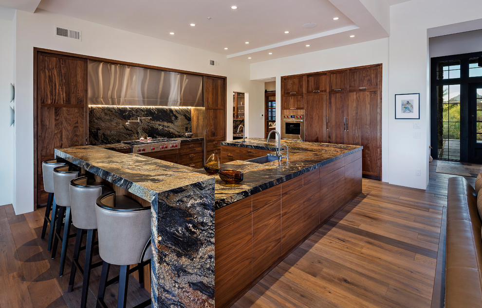 Kitchen in Phoenix with a farmhouse sink, dark wood cabinets, stone slab splashback, stainless steel appliances and medium hardwood floors.